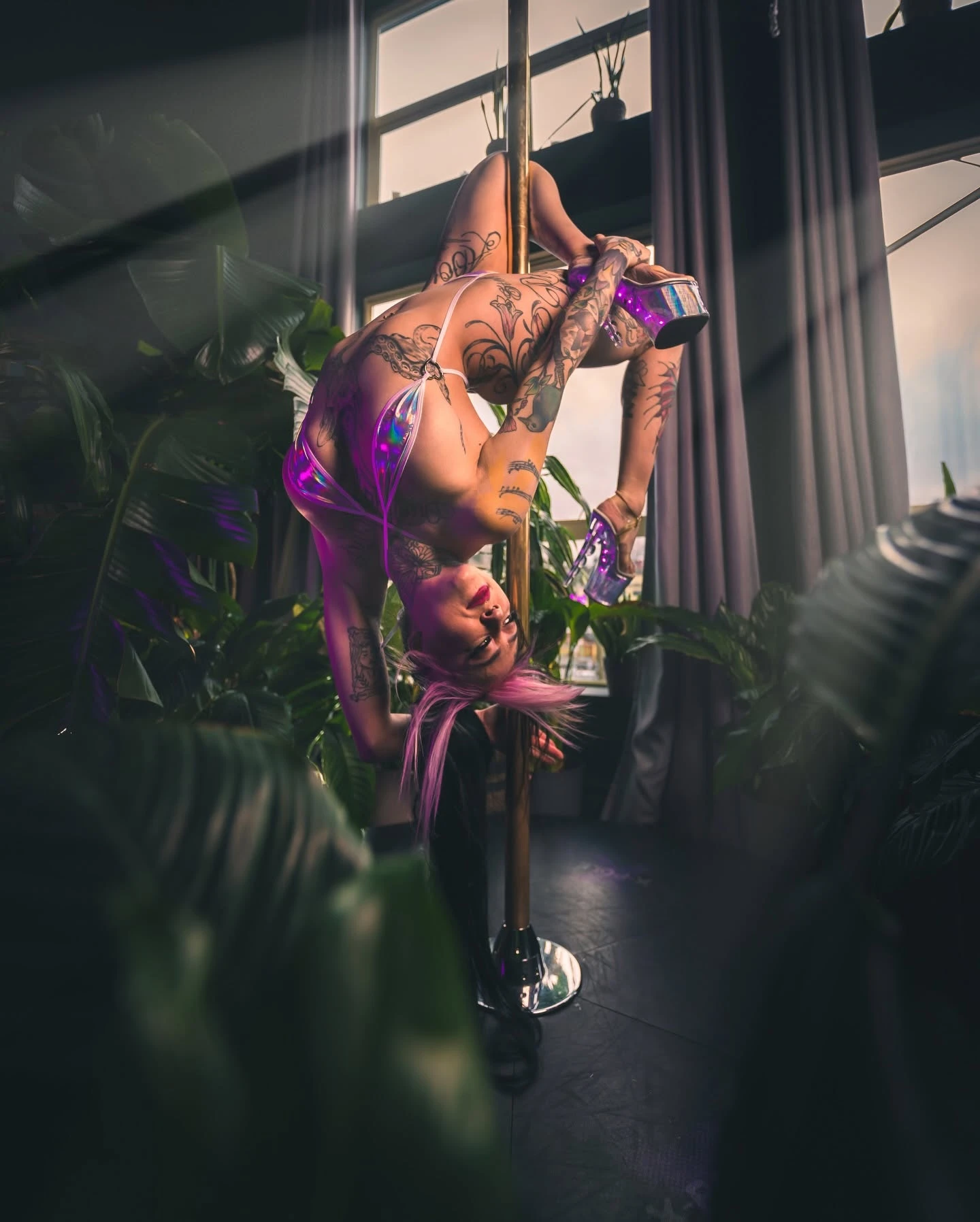AKASHAH performing an inverted pole pose surrounded by plants